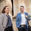 A woman and a man in business wear walking past a sandstone building